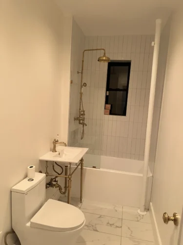 Bathroom renovation in progress in a Manhattan apartment, with white tile, bathtub, brass fixtures and console sink.