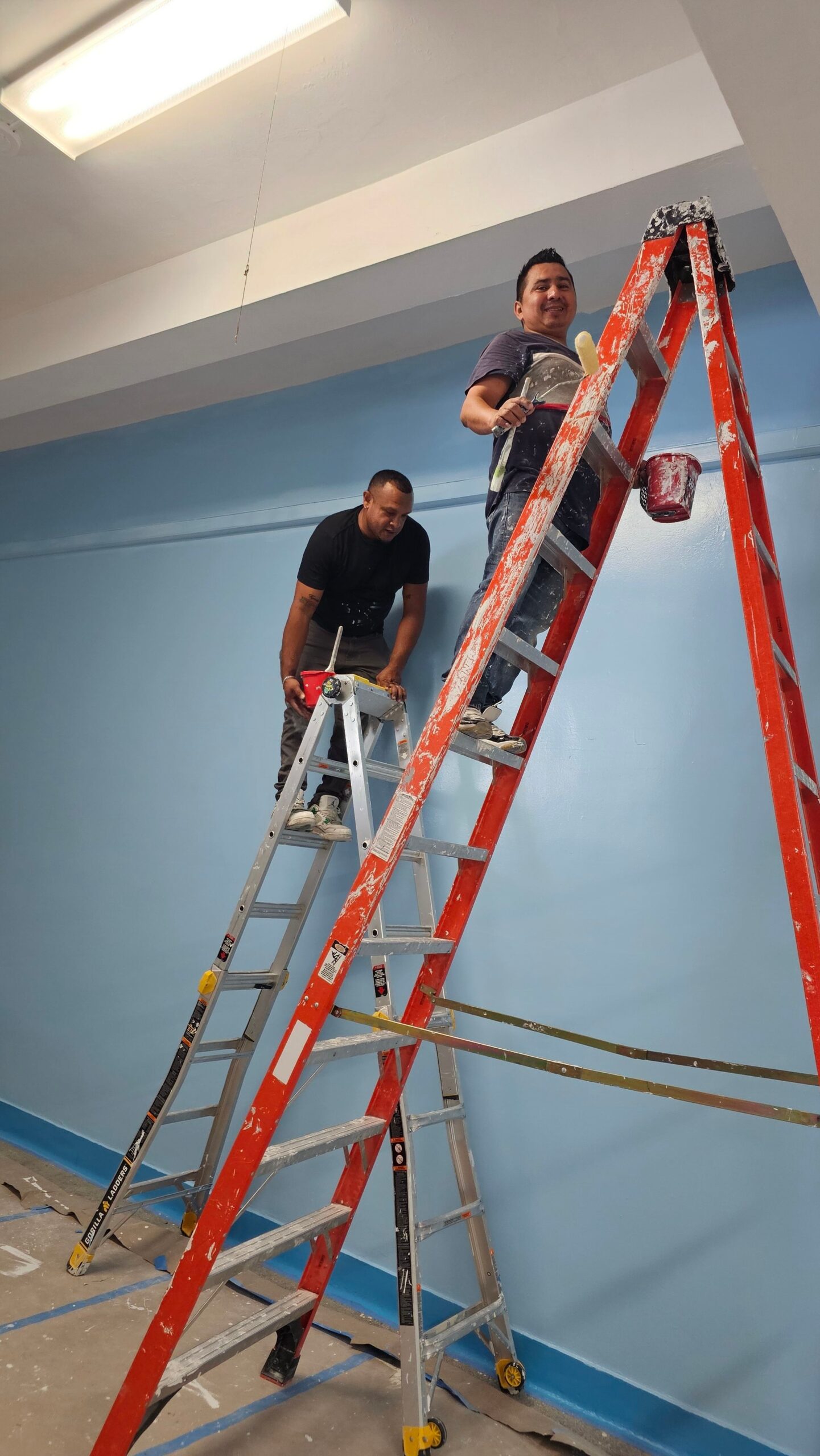 Corniel team members performing interior wall finishing on ladders.